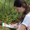 a woman doing fieldwork on papers in her hand while in the woods